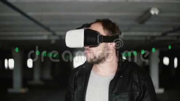 年轻人站在停车场用虚拟现实眼镜用VR耳机探索空间4K视频的预览图