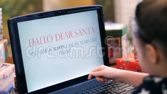 穿着漂亮裙子的可爱的金发女孩正在笔记本电脑上打印一封给圣诞老人的信信靠近一棵圣诞树上面装饰着视频的预览图