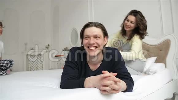 快乐的家庭穿睡衣在卧室里很有趣两个微笑的成年人和快乐的男孩正在玩白色游戏视频的预览图