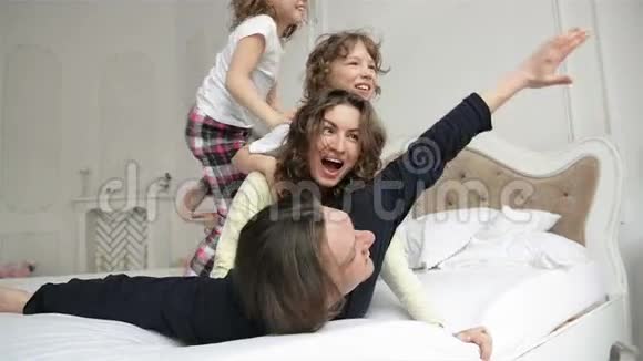 快乐的家庭穿睡衣在卧室里很有趣两个有卷发的儿童和一对年轻夫妇视频的预览图