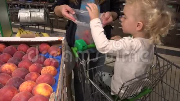 可爱的小女孩在购物车上帮助妈妈在超市里摘桃子水果视频的预览图