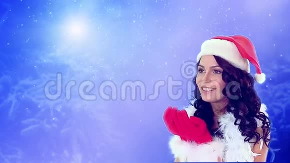戴着圣诞帽的女孩在蓝色的雪背景上吹着飞舞的雪花视频的预览图