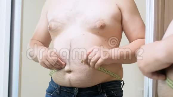 4k视频超重男子试图用黄色测量带在镜子上测量他的大肚子视频的预览图