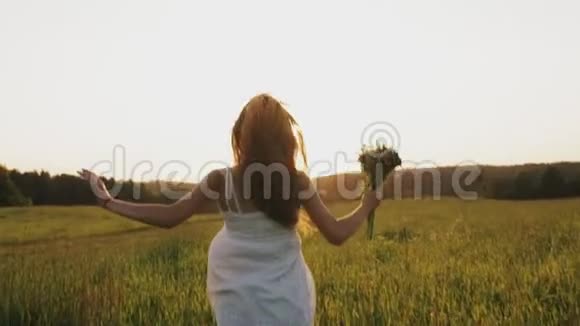 日落时分带着花束的女孩在乡间田野里奔跑在阳光下的草地上尽情享受视频的预览图