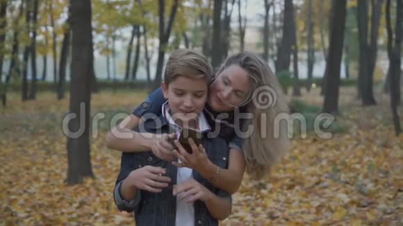 妈妈和儿子一起在秋季公园的智能手机上自拍视频的预览图