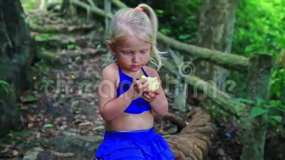 特写小金发女孩在丛林中吃大苹果视频的预览图