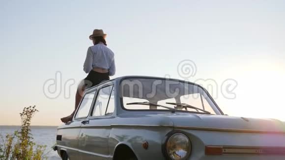在阳光下的复古车车顶上年轻的女性手里拿着一个杯子在老式汽车上视频的预览图