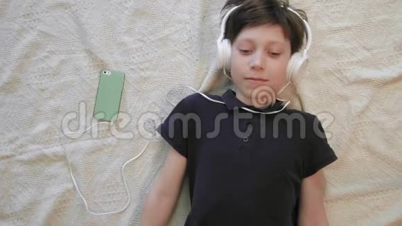 戴着智能手机耳机听音乐的可爱小男孩的俯视图视频的预览图
