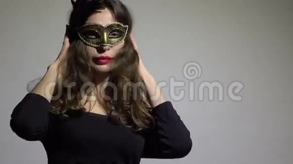 神秘的黑发女人戴着狂欢节面具在灰色背景下摆姿势4K视频视频的预览图