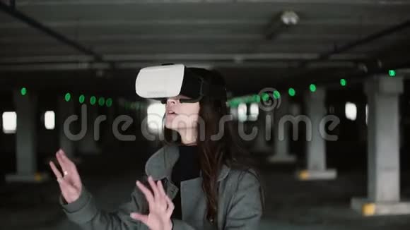 年轻女子在停车处使用虚拟现实眼镜女孩触摸空间与手戴VR耳机4K视频的预览图