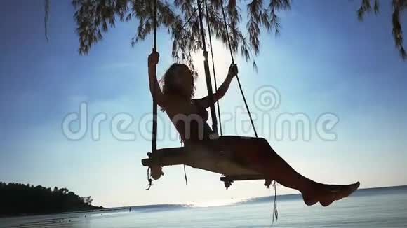 美丽的快乐女孩戴着太阳镜和比基尼在海滩上的秋千上放松慢动作1920x1080视频的预览图