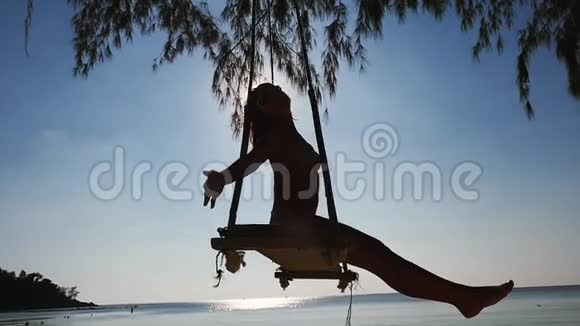 戴太阳镜的漂亮女孩在海滩的秋千上放松穿着热带海洋比基尼的女人慢动作视频的预览图