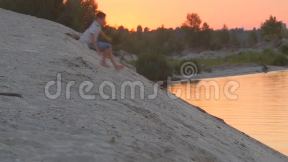 可爱的男孩在日落时从一座沙丘上跑和跳孩子的积极休息视频的预览图
