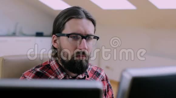 戴眼镜的胡子男有两台显示器在办公室工作视频的预览图