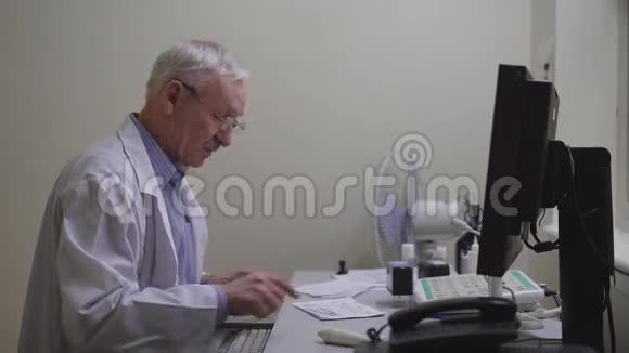 男性医生用电脑穿制服坐办公室和使用电脑的高级男性医生的侧面视图视频的预览图