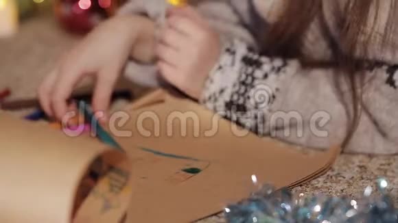 一个漂亮的小女孩在一棵装饰精美的圣诞树附近画了一幅圣诞老人的画特写镜头手工艺品视频的预览图
