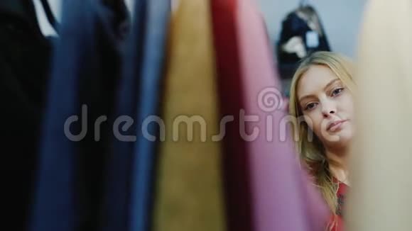愉快的购物一个年轻的成年女人的肖像看着商店里衣架上的衣服女人衣服视频的预览图
