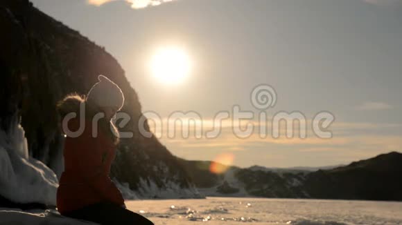 日落时女孩坐在冰冻的湖岸上视频的预览图