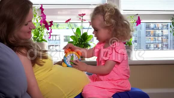 孕妇和可爱的女儿在肚子上玩玩具钟视频的预览图