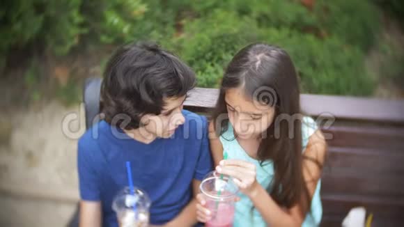 男孩和女孩少年坐在长凳上手里拿着带着新鲜和冰沙的眼镜4k慢动作视频的预览图