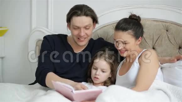 可爱的小女儿正在读一本预言语言的书躺在床上她的父母在嘲笑一些人视频的预览图
