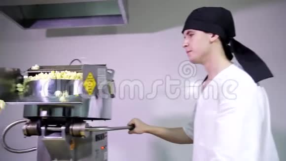 年轻有魅力的男厨房工作人员戴着黑色头巾闻着香味等待着工作爆米花自动机视频的预览图