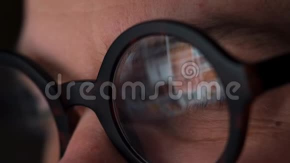 戴眼镜的人看着显示器和上网监视器屏幕反映在眼镜上视频的预览图