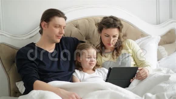 现代家庭正在使用电子小玩意一起躺在床上帅哥美女和可爱的小女孩视频的预览图