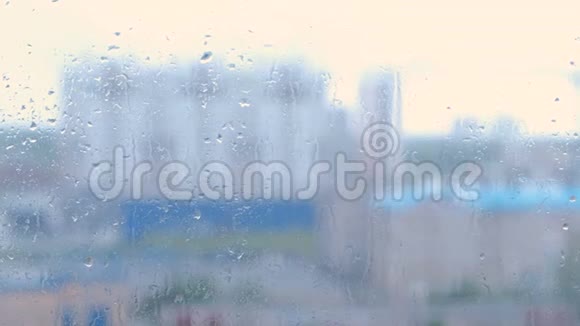 雨滴沿着窗户的特写从潮湿的窗户看多栋楼的房子模糊视频的预览图