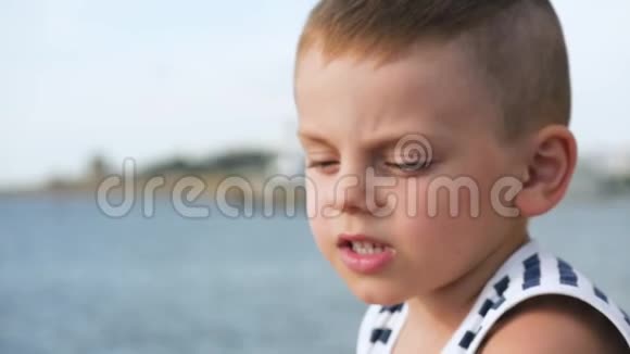 穿着水手条纹衬衫的小男孩眯着眼睛看着远处天空和大海的背景视频的预览图