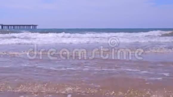 阳光充足的沙滩上有长而大的波浪和码头的海岸视频的预览图