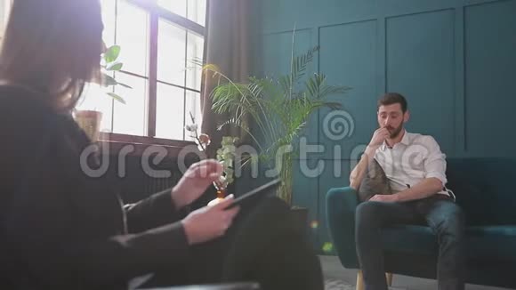 女性心理学家在蓝色办公室内部的心理会话中倾听男性客户的意见视频的预览图