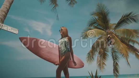 快乐美丽的女人带着粉红色的冲浪板走到海滩视频的预览图