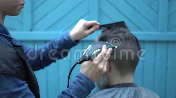 女理发师在理发厅为留胡须的男理发师理发理发时使用电动剃须刀和梳子视频的预览图