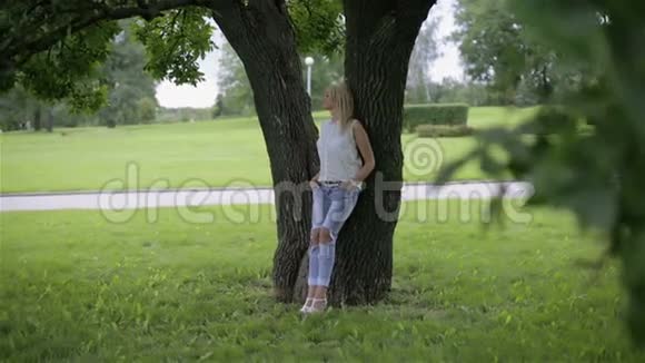 一个女孩斜倚在公园的一棵树上视频的预览图