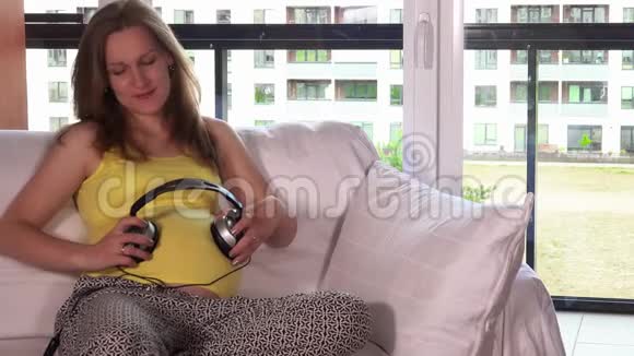孕妇戴着耳机在客厅听音乐视频的预览图