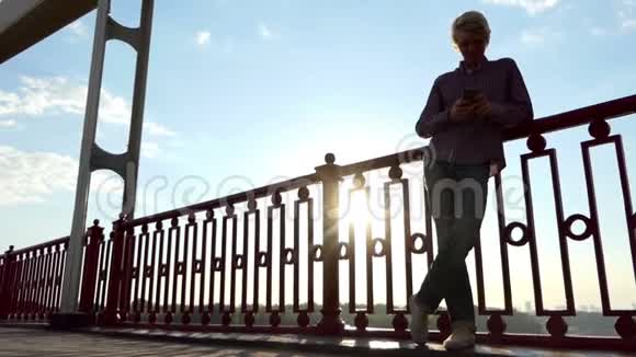 年轻的金发碧眼的男人在斯隆莫的一座移动的河桥上享受着灿烂的日落视频的预览图