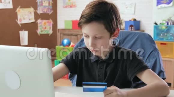 可爱的小男孩在网上购物用笔记本电脑输入信用卡号码并在制作后快乐视频的预览图
