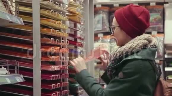 年轻的艺术家女士在艺术家商店里选择彩色纸视频的预览图