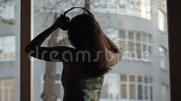 迷人的年轻女子带着耳机在窗边跳舞视频的预览图