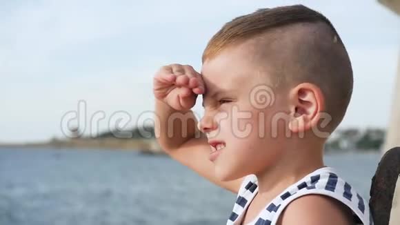 穿着水手条纹衬衫的小男孩眯着眼睛看着远处天空和大海的背景视频的预览图