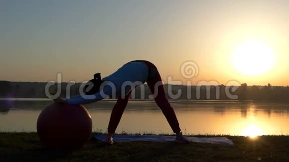 一个苗条的女人站着在日落时滚动她的健身球视频的预览图