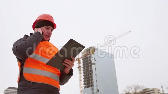 建筑设计师男工在手机智能手机上用头盔和橙色背心交谈背景是一个多人视频的预览图