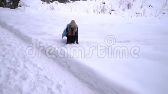 年轻漂亮的女孩走在白雪皑皑的冬林里她既快乐又开朗女孩扔雪慢动作视频的预览图
