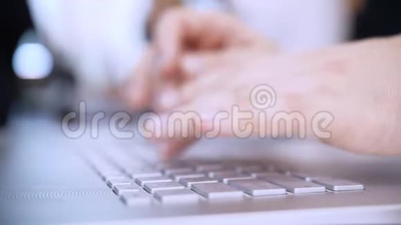 特写镜头手在笔记本电脑键盘上工作在后台办公室工作离焦视频的预览图