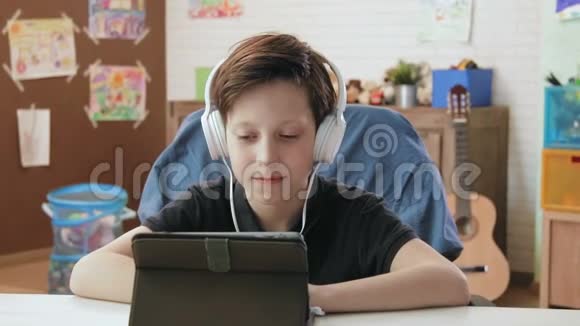 可爱的小男孩用数码平板电脑看有趣的视频戴着耳机视频的预览图