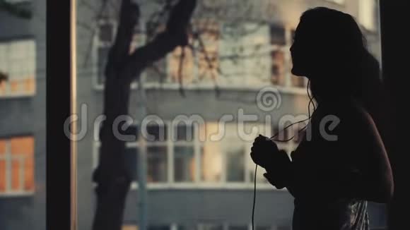 迷人的年轻女子带着耳机在窗边跳舞视频的预览图