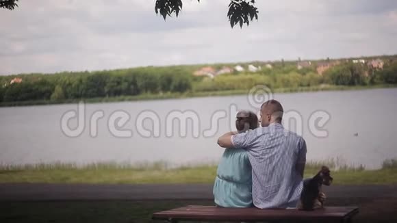 一对恋爱中的情侣坐在河边的一张桌子上那个家伙在拥抱那个女孩一只小狗坐在旁边视频的预览图