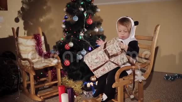 小孩坐在圣诞树旁的椅子上婴儿正在打开圣诞礼物视频的预览图