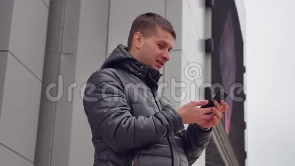 男人在你的智能手机上输入短信在户外夹克里看屏幕冬天视频的预览图